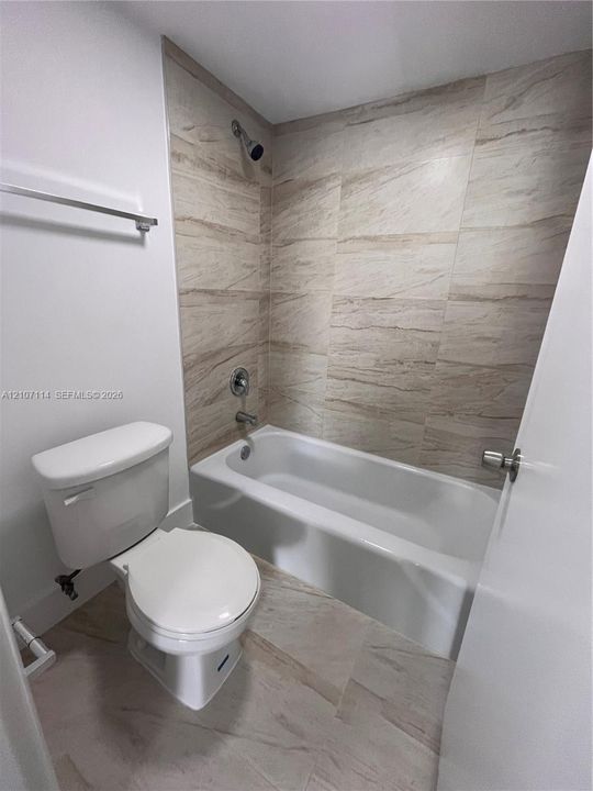 Bathroom featuring a white porcelain tub, neutral-toned tile surround, matching floor tiling, and a white toilet