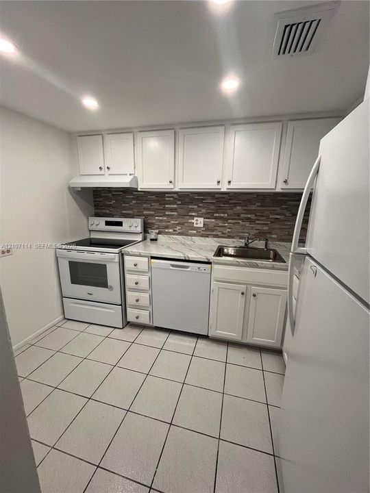 Kitchen featuring white cabinetry, stone-patterned countertops, mosaic tile backsplash, recessed lighting, and tiled flooring