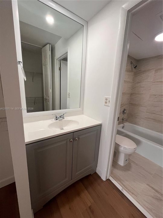 Bathroom featuring a grey vanity with a solid surface countertop, large wall-mounted mirror, wood-finish flooring, and a tiled shower-tub combination