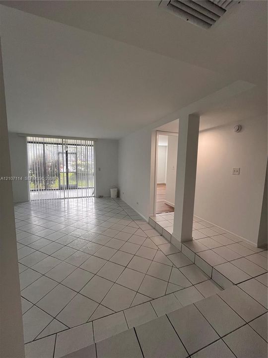 Open-concept floor plan featuring diagonal-set ceramic tile flooring, a multi-level layout with a raised platform, and floor-to-ceiling vertical blinds