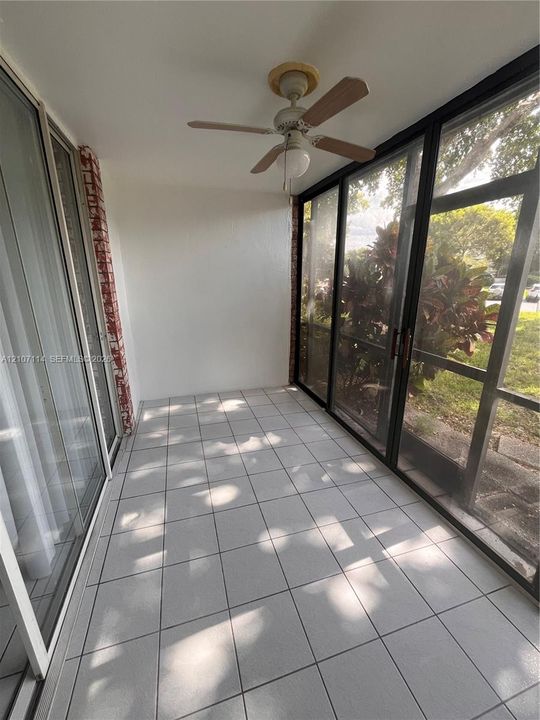 Enclosed patio featuring tile flooring, a ceiling fan, sliding glass doors, and a decorative brick accent pillar