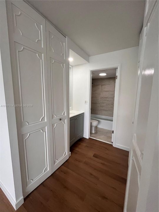 Floor-to-ceiling cabinetry with decorative molding, wood-finish flooring, and a vanity cabinet featuring a solid-surface countertop