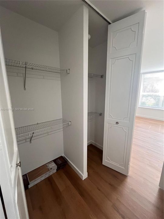 Dual reach-in closet featuring white paneled bifold doors and metal wire shelving, complemented by wood-finish flooring