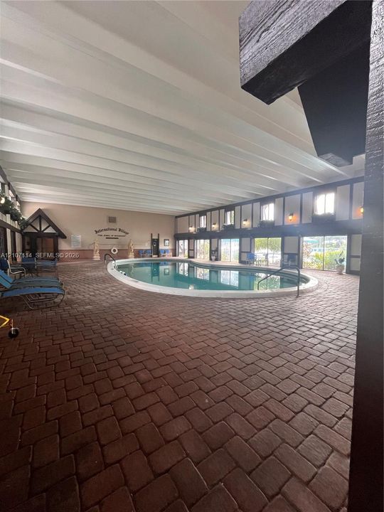 Indoor pool area featuring a brick-paved deck, exposed white ceiling beams, timber-style wall accents, and wall-mounted lighting fixtures