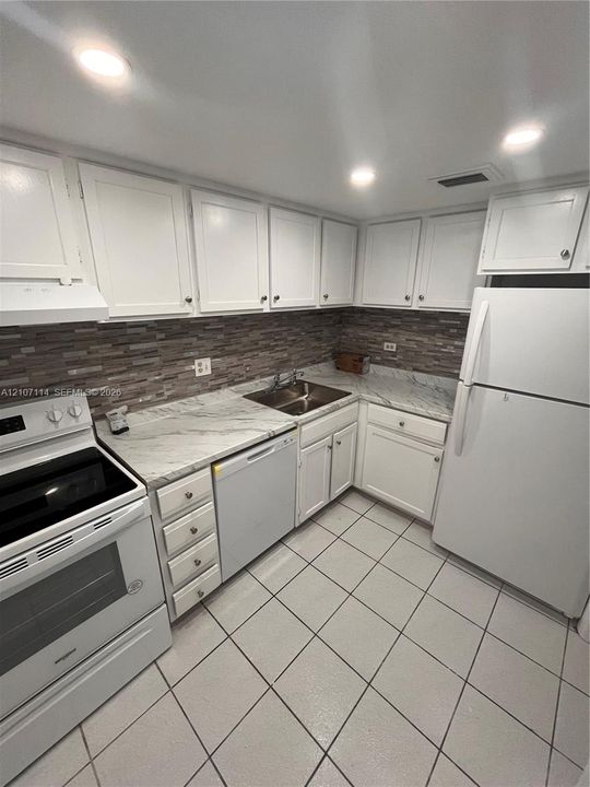 Kitchen featuring white shaker-style cabinetry, stone-patterned laminate countertops, a decorative linear-tile backsplash, stainless steel double-basin sink, and ceramic tile flooring