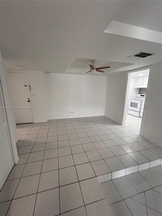 Open-concept interior featuring oversized tile flooring, a tray ceiling with a center-mounted ceiling fan, and multi-level floor elevation