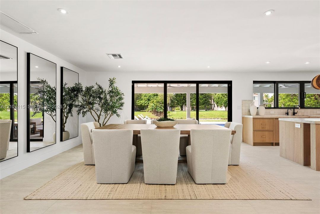 Open-concept interior featuring large-format tile flooring, recessed ceiling lighting, wall-to-wall mirrors, and multi-panel sliding glass doors opening to a covered patio