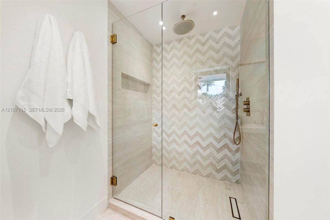 Walk-in shower featuring a chevron-patterned tile accent wall, glass enclosure, recessed wall niche, rainfall showerhead, and a handheld fixture