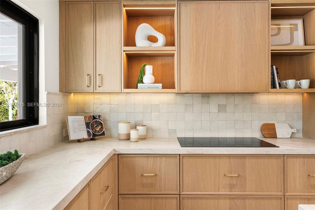 Custom wood cabinetry with integrated open shelving, stone countertops, square-tile backsplash, built-in cooktop, and under-cabinet lighting