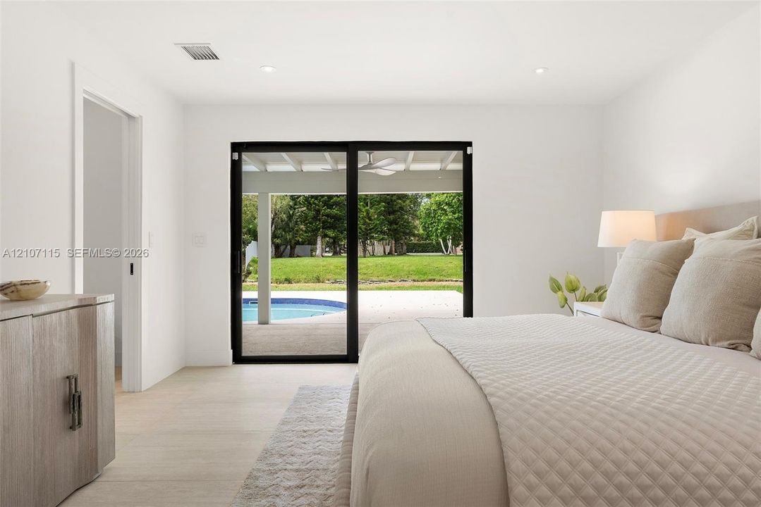 Light-filled interior featuring sliding glass doors with black frames, neutral stone-finish flooring, and recessed lighting