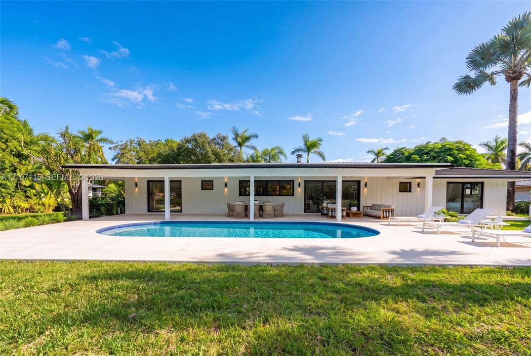 Expansive rear patio featuring a swimming pool, covered lanai, vertical exterior siding, and sliding glass doors