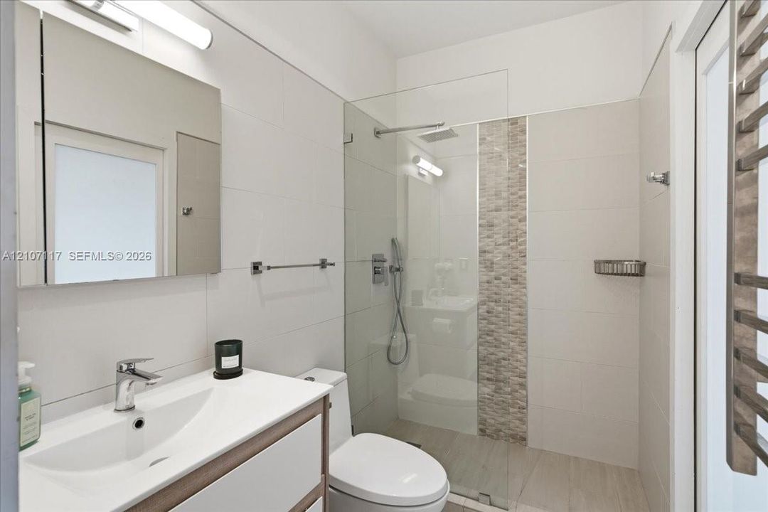 Bathroom featuring a vanity with integrated sink, frameless glass-enclosed shower with tiled decorative inlay, wall-mounted medicine cabinet, and polished chrome fixtures