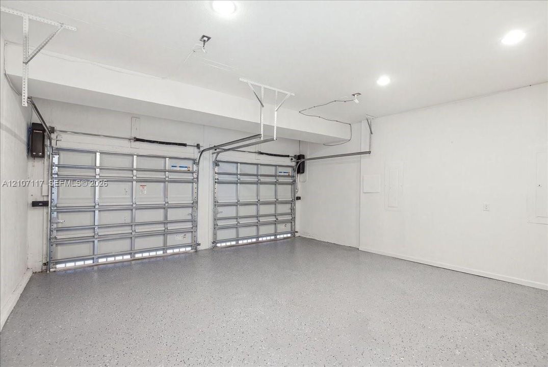 Two-car garage featuring finished epoxy flooring, white walls, and recessed lighting