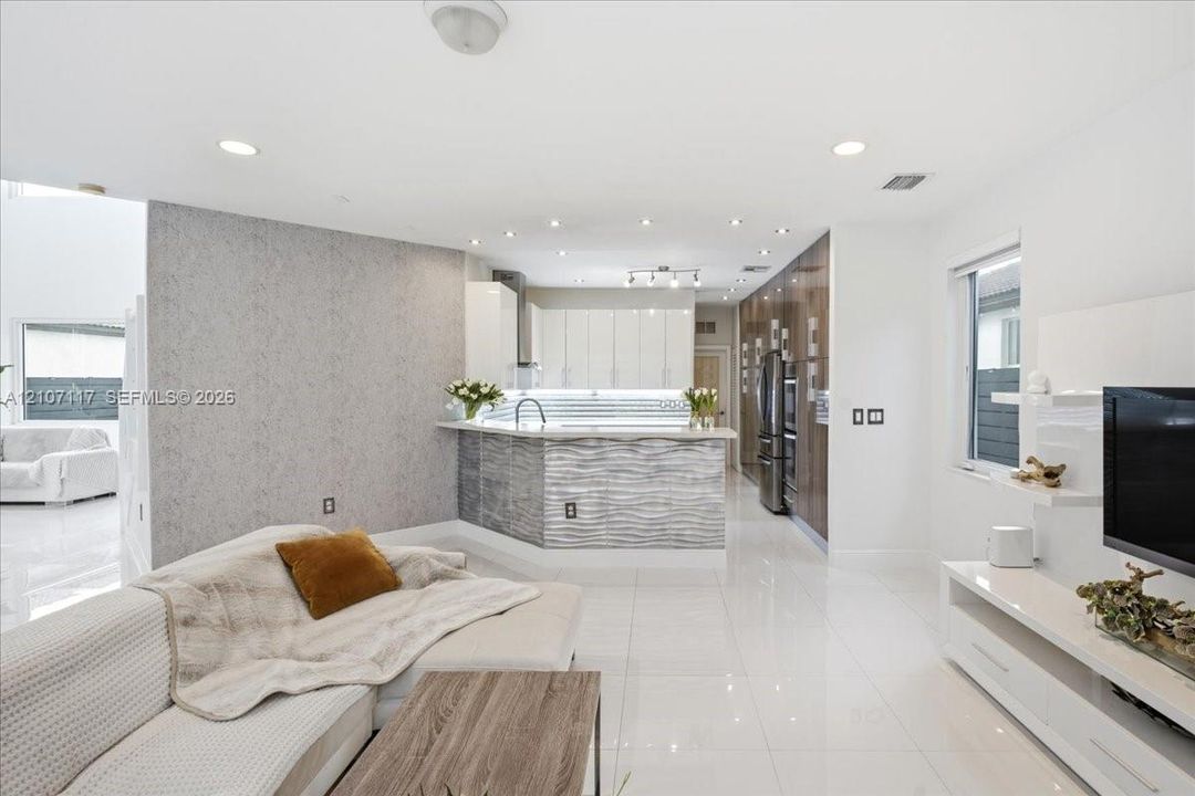 Open-concept kitchen featuring high-gloss cabinetry, a textured stone-finish island, integrated stainless steel appliances, recessed ceiling lighting, and polished tile flooring