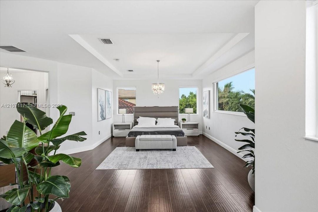 Spacious room featuring wood-finish flooring, a recessed tray ceiling, large picture windows, and a crystal-style chandelier