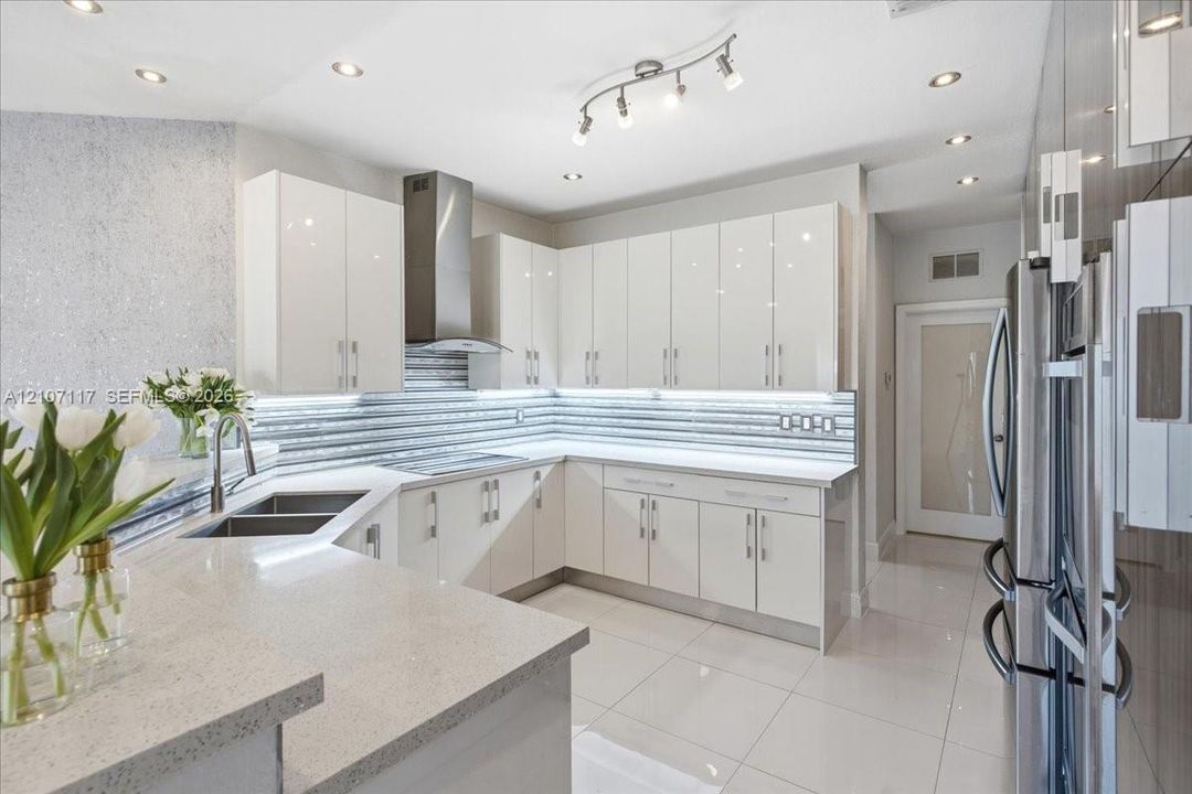 Kitchen featuring high-gloss white cabinetry, quartz countertops, horizontal textured tile backsplash, stainless steel range hood, and large-format porcelain tile flooring