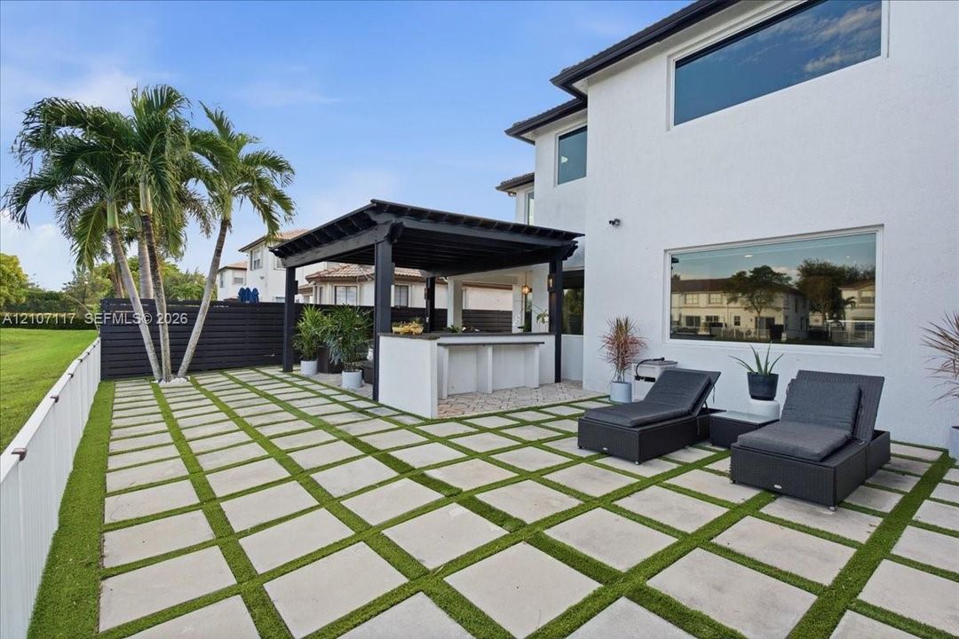 Outdoor living area featuring a covered pergola, integrated bar counter, large-format paver patio with turf inlay, and horizontal slat privacy fencing