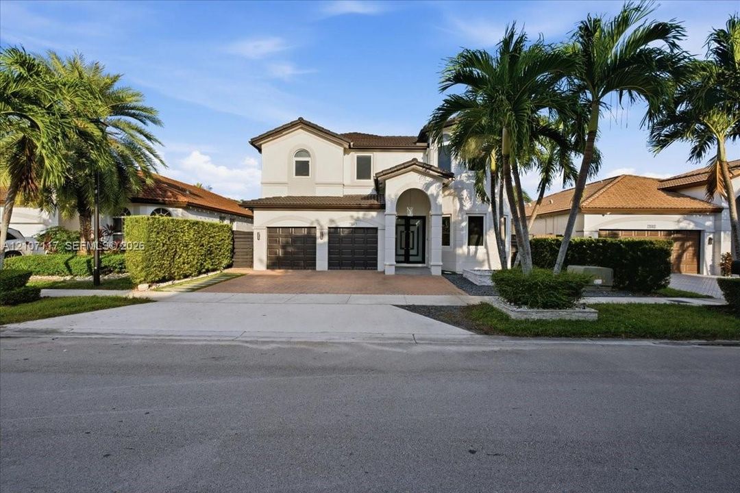 Two-story stucco exterior featuring a tiled roof, arched entryway, paved driveway, and multiple palm trees