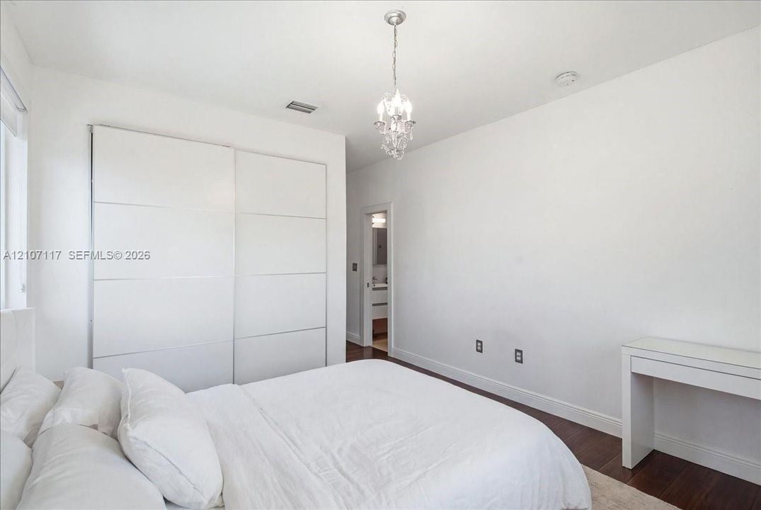 Room featuring dark wood-finish flooring, floor-to-ceiling built-in sliding door wardrobe, and a crystal chandelier