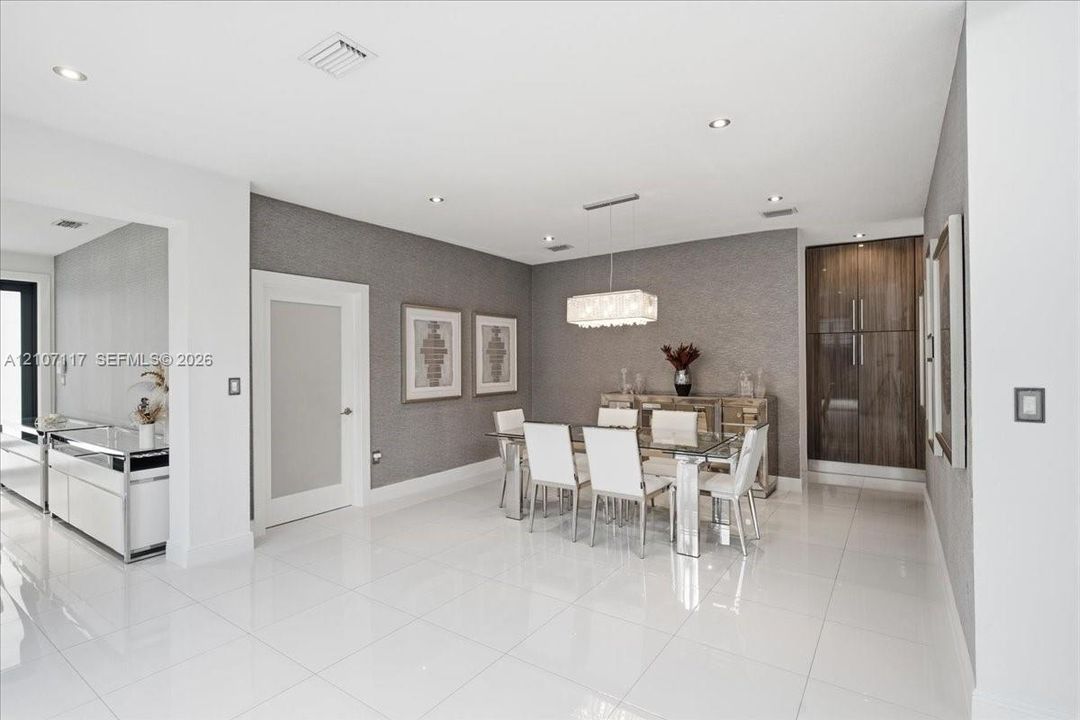 Open-concept interior featuring large-format polished tile flooring, textured wall coverings, a modern rectangular chandelier, and built-in full-height wood-finish cabinetry