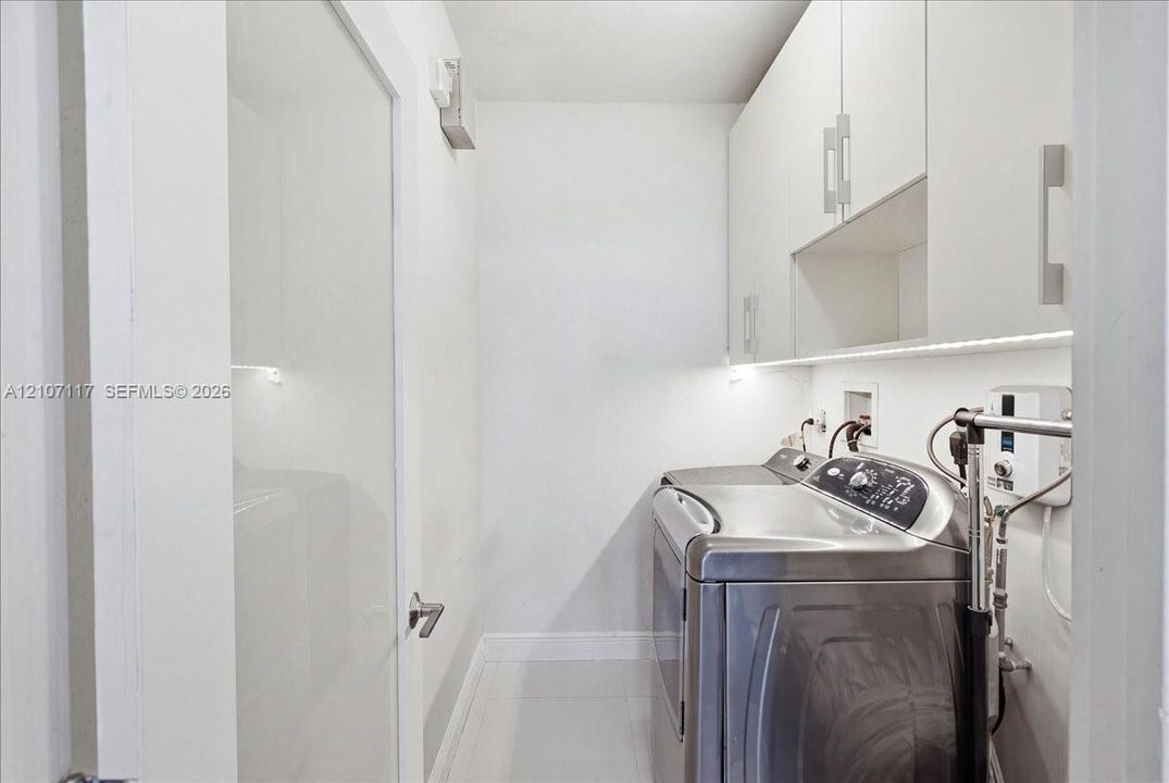 Laundry area featuring flat-panel white cabinetry, under-cabinet task lighting, polished tile flooring, and a solid-core interior door with modern lever hardware