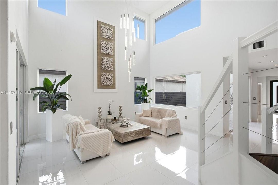 Double-height living area featuring floor-to-ceiling windows, polished tile flooring, contemporary multi-pendant lighting, and a staircase with stainless steel cable railing