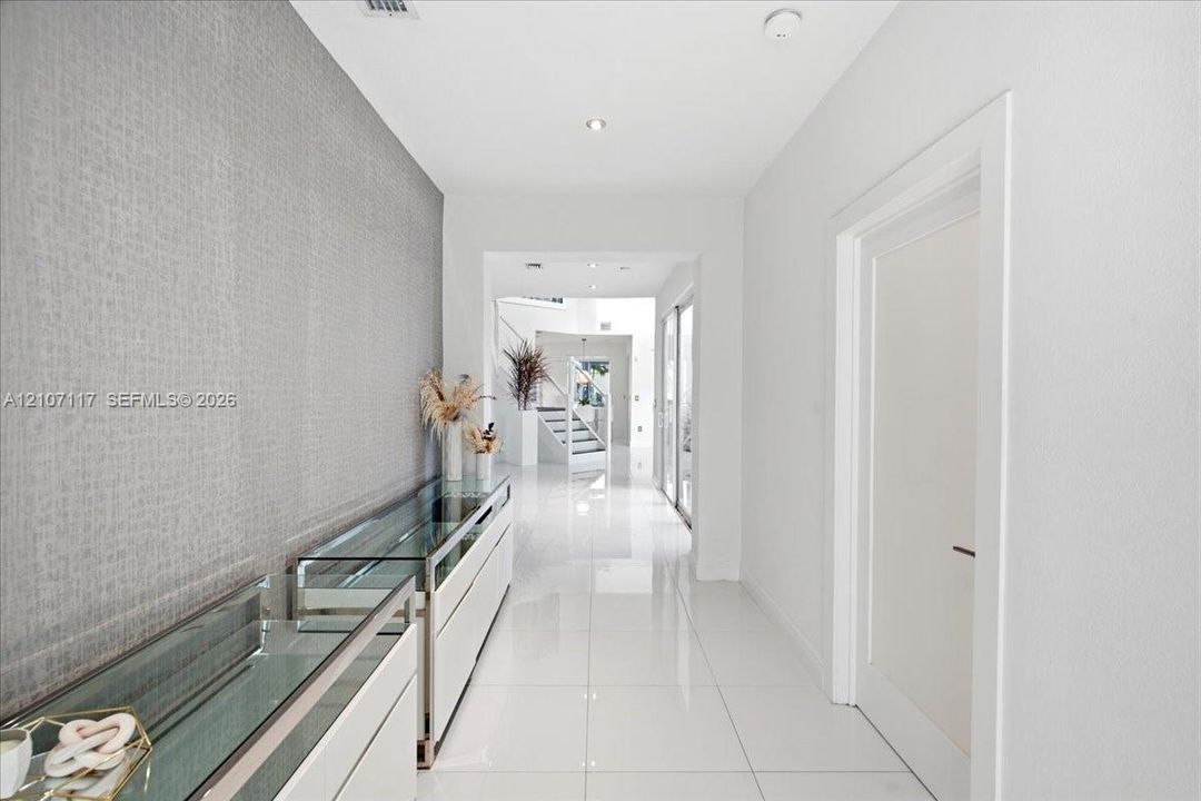 Hallway featuring polished white tile flooring, recessed lighting, and a textured grey accent wall