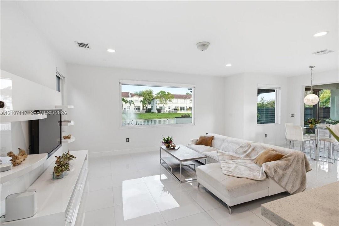 Open-concept living space featuring high-gloss tile flooring, recessed lighting, built-in media shelving, and large windows with water exposure