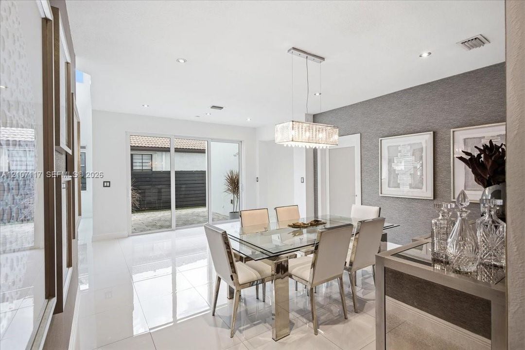Dining area featuring polished large-format tile flooring, a rectangular multi-light glass pendant fixture, textured grey accent wall, and sliding glass doors
