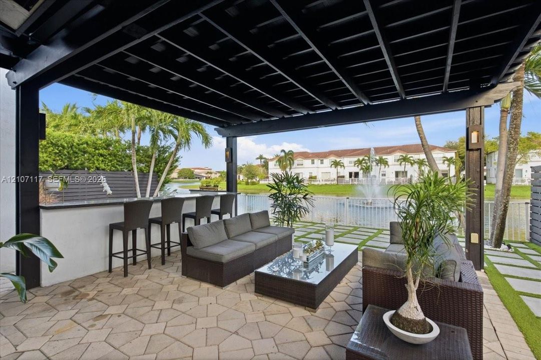Covered patio featuring a black pergola, stone paver flooring, and a built-in outdoor bar with a stone countertop