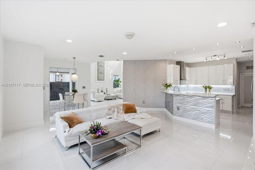 Open-concept interior featuring large-format tile flooring, high-gloss kitchen cabinetry, a textured stone feature wall, and a raised breakfast bar with horizontal wave-patterned paneling