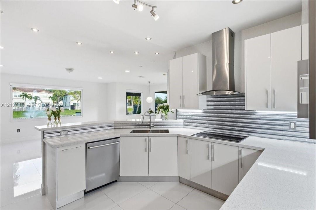 Contemporary kitchen featuring flat-panel white cabinetry, light-toned countertops, a textured metal backsplash, stainless steel appliances, and large-format floor tiling