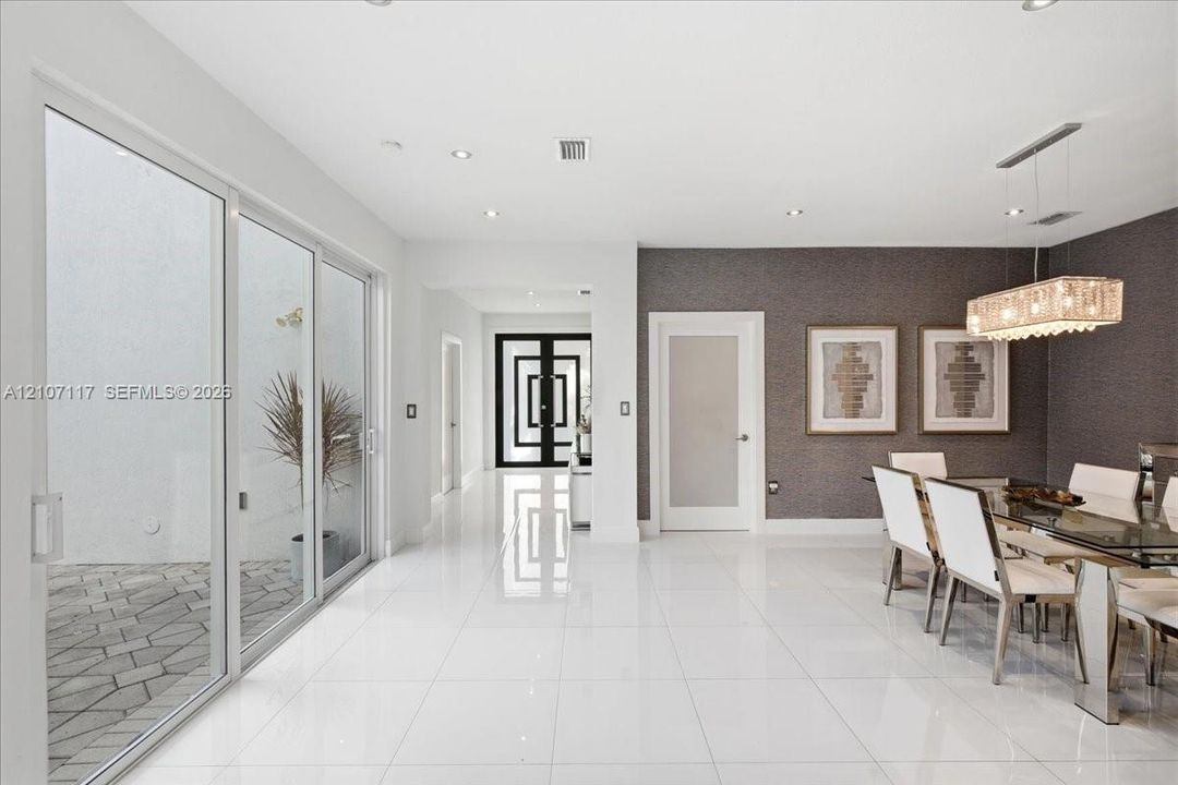 Large-format white tile flooring, floor-to-ceiling glass sliding doors, recessed lighting, textured accent wall, and geometric-patterned entry door