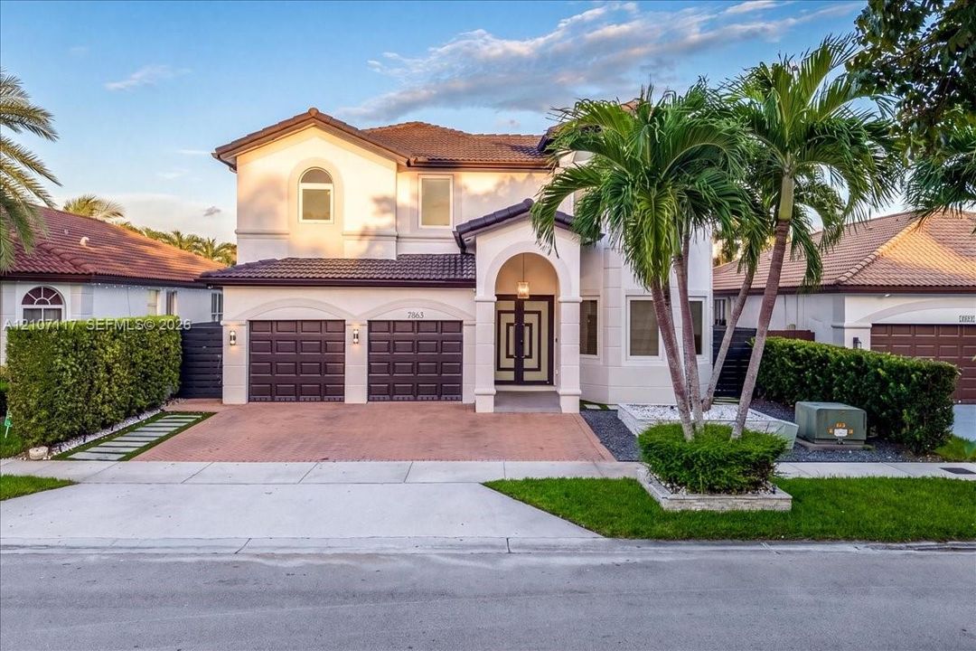 Two-story residence featuring a tile roof, paved driveway, three-car garage, arched covered entryway, and double-entry doors