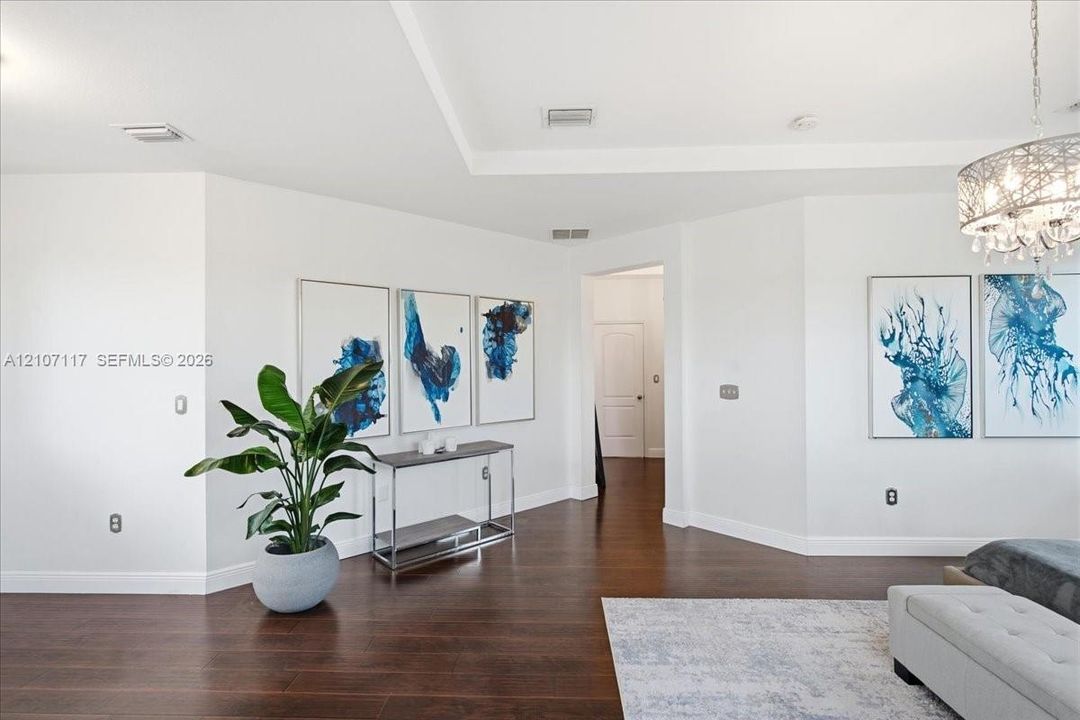 Interior space featuring dark wood-finish flooring, recessed tray ceiling, and a decorative crystal-style chandelier