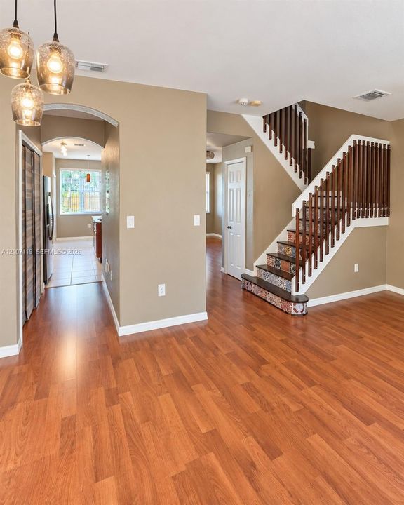 Wood-finish flooring, staircase with patterned risers and wood handrail, trio of glass pendant lights, and arched entryway