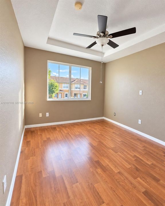Tray ceiling with a central multi-blade ceiling fan and wood-finish flooring