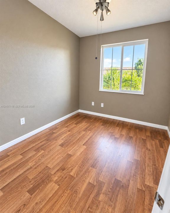 Room featuring wood-finish flooring, neutral-toned wall paint, a multi-pane sliding window, and a three-bulb flush-mount light fixture