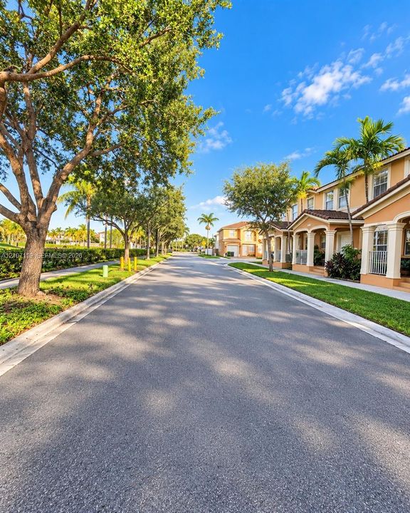 Residential streetscape featuring multi-story dwellings with stucco exteriors, arched covered entrances, concrete tile roofing, and mature landscaping