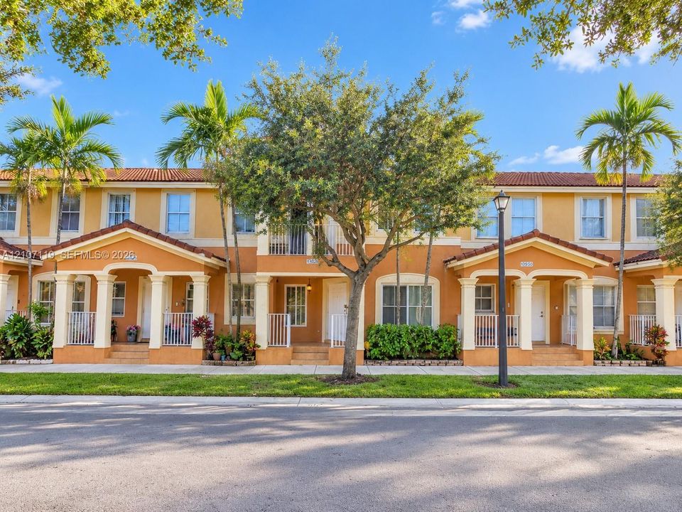 Mediterranean-style townhome exterior featuring a red tile roof, arched entryway columns, second-story balconies, and private covered porch entries