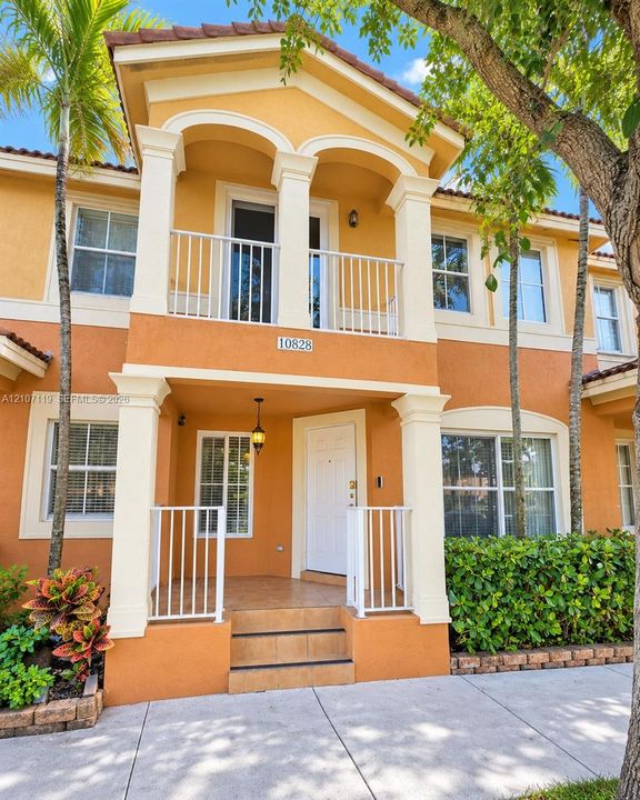 Stucco exterior featuring dual-level covered porches with white railing, decorative architectural columns, and tiled entry steps