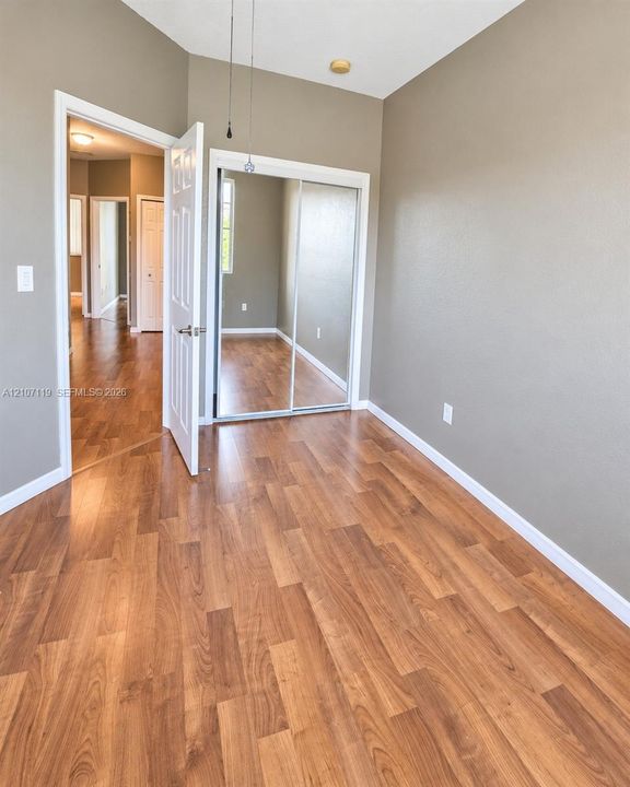 Room featuring wood-finish flooring, neutral wall paint, and closet with sliding mirrored doors