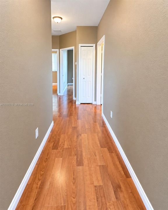 Hallway featuring wood-finish flooring, neutral wall paint, and white bi-fold closet doors