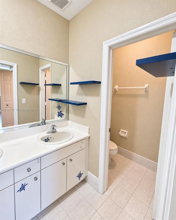 White vanity with integrated basin, solid-surface countertop, full-width mirror, and ceramic tile flooring