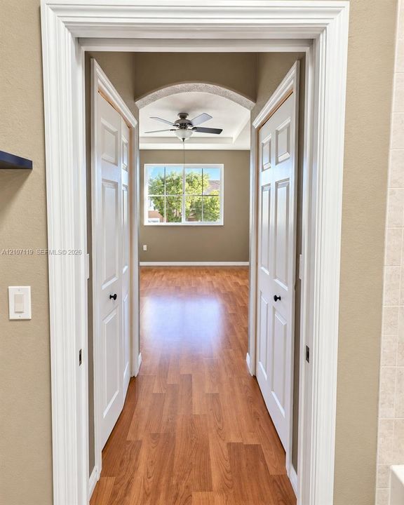 Arched doorway with white casing, wood-finish flooring, two six-panel swing doors, and a ceiling fan with integrated lighting