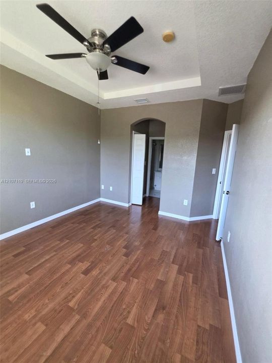 Room featuring a recessed tray ceiling, wood-finish flooring, and a ceiling-mounted fan with integrated lighting