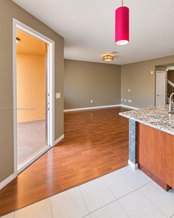 Kitchen featuring stone-finish countertops, wood-finish cabinetry, and ceramic tile flooring, complemented by wood-finish flooring and a cylindrical pendant light fixture