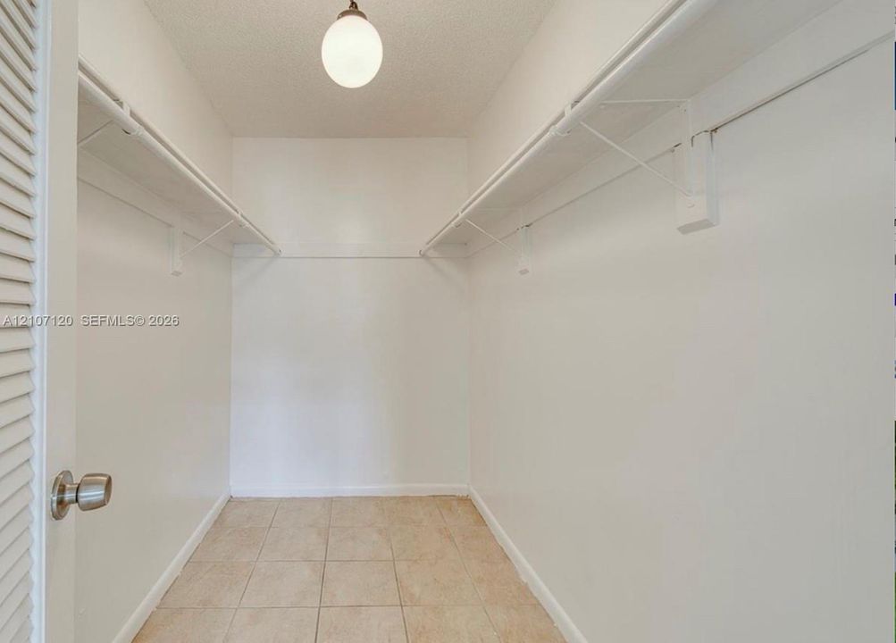Storage space featuring white walls, tiled flooring, dual-level wire shelving, and a globe-style overhead light fixture