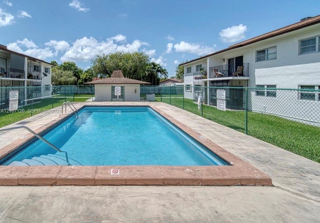 In-ground swimming pool featuring a concrete deck, metal perimeter fencing, and a detached poolside structure