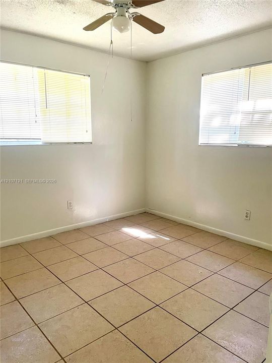 Room featuring large-format neutral floor tile, dual-aspect windows, and a ceiling fan with integrated lighting